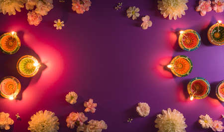 Happy Diwali - Clay Diya lamps lit during Dipavali, Hindu festival of lights celebration. Colorful traditional oil lamp diya and flowers on purple backgroundの写真素材
