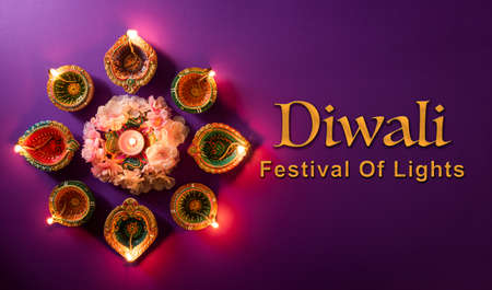 Happy Diwali - Clay Diya lamps lit during Dipavali, Hindu festival of lights celebration. Colorful traditional oil lamp diya with the text on purple backgroundの写真素材