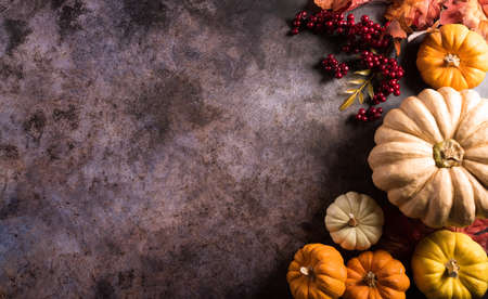 Thanksgiving background concept with fall leaves, pumpkin and seasonal autumnal decor on dark stone background, top view, copy space.の写真素材