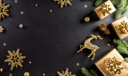 Christmas and new year background concept. Top view of Christmas gift box, spruce branches, pine cones, reindeer, christmas ball and snowflake on black wooden background.の写真素材