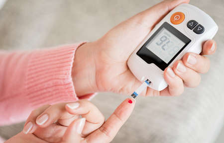 Close up woman hands checking blood sugar level by glucose meter for diabetes tester using as medicine, glycemia, healthcare and medical concept.の写真素材