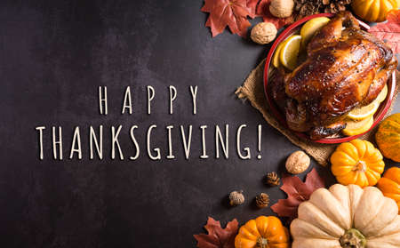 Thanksgiving dinner background concept with turkey roasted and all sides dishes, fall leaves, pumpkin and seasonal autumnal decor on dark stone background, top view, copy space.の写真素材