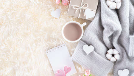 Love and Valentine's day decoration concept. Pink paper hearts with gift box , coffee cup and beige sweater on cream colour knitted blanket and fluffy background.の写真素材