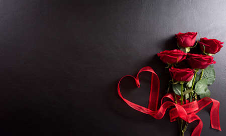 Love and Valentine's day concept made from red rose  and heart ribbon on black wooden background. Top view with copy space, flat lay.の写真素材