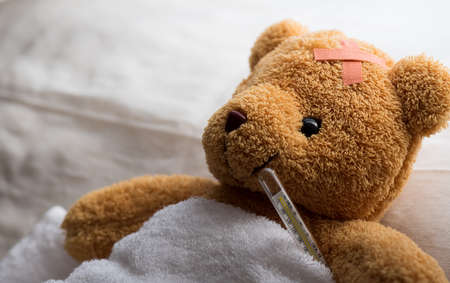 Teddy bear lying sick in hospital bed with with thermometer and plaster. Healthcare and medical concept.の写真素材