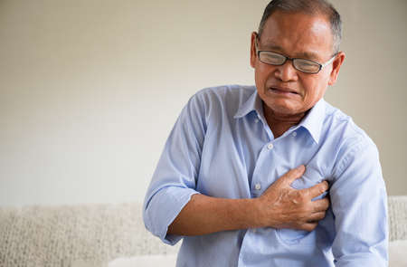 Close Up senior male asian suffering from bad pain in his chest heart attack at home. Healthcare and medical concept of senior heart disease.の写真素材