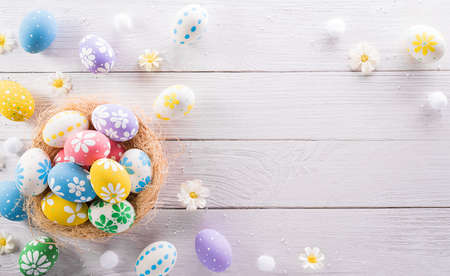 Happy easter! colourful Easter eggs in a nest with flower on white wooden background.の写真素材