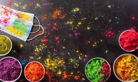 Top view of colorful holi powder with multicolored medical mask holi paint on dark background. Happy holi festival during coronavirus 
 (Covid-19) pandemic concept.の写真素材