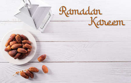 Top view image of Ramadan Kareem decoration, dates fruit and rosary beads with the text on white wooden background.の写真素材