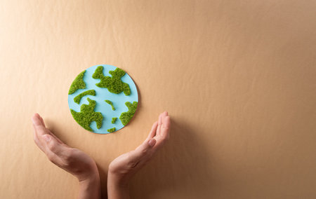 Hands holding paper earth with grass on brown background. World environment day, earth day and save earth concept.の写真素材