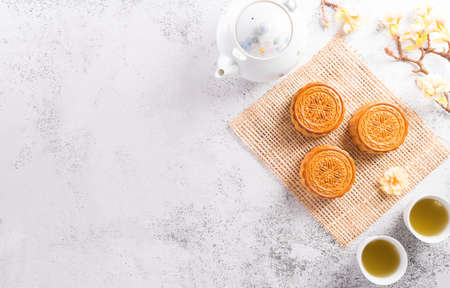 Chinese Mid-Autumn Festival concept made from mooncakes, tea and plum blossom on white stone...