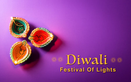 Happy Diwali - Clay Diya lamps lit during Dipavali, Hindu festival of lights celebration. Colorful traditional oil lamp diya on purple backgroundの写真素材