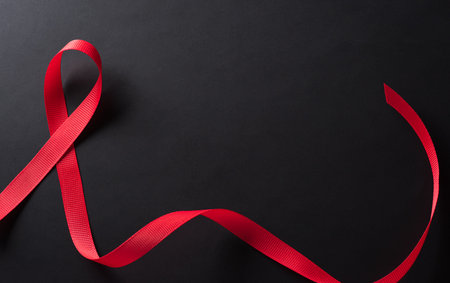 Closeup red ribbon HIV, world AIDS day awareness ribbon on black background. Healthcare and medicine concept.の写真素材
