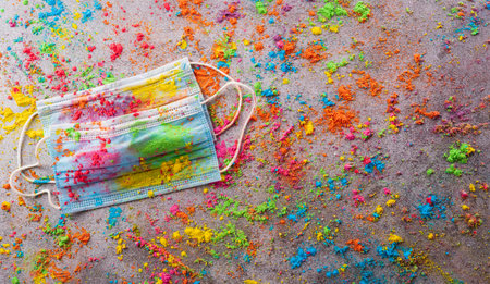 Top view of colorful holi powder with multicolored medical mask holi paint on dark background. Happy...