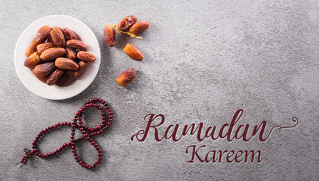 Top view of Ramadan Kareem decoration, dates fruit, rosary beads and the text on dark stone background.の写真素材