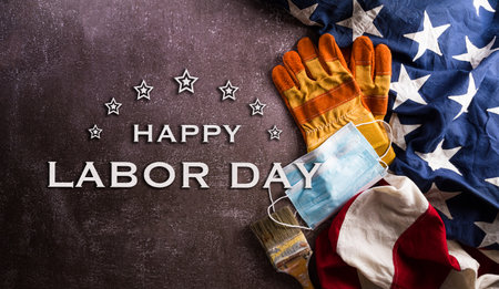 Happy Labor day concept during coronavirus disease (Covid-19). American flag with different construction tools and medical mask on dark stone background.の写真素材