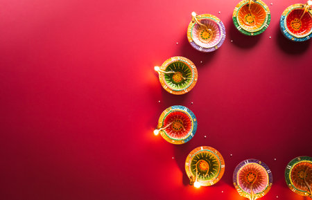 Happy Diwali - Clay Diya lamps lit during Diwali, Hindu festival of lights celebration. Colorful traditional oil lamp diya on red backgroundの写真素材