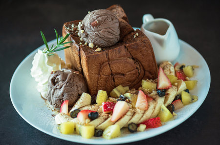 Plate of french toast topped with chocolate ice cream, mixed berries, banana and maple syrup and  on dark background.の写真素材