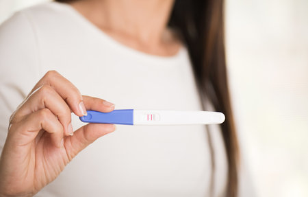 Woman with pregnancy test positive result, focus on foreground 2 stripes.の写真素材