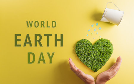 Hands holding green heart with watering on yellow background. World environment day, earth day, save earth and eco concept.の写真素材