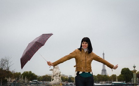 Young smiling brunette on vacation in Paris France holding umbrella in her hands. Eiffel tower is visible on background.の写真素材