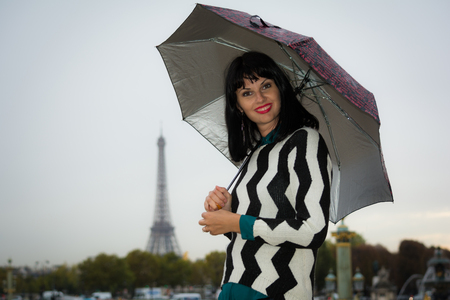 Young smiling brunette on vacation in Paris France holding umbrella in her hands. Eiffel tower is visible on background.の写真素材