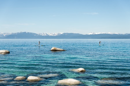 People standing on SUP rowing along Lake tahoe shorelileの写真素材