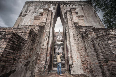 Traveler taking picture of Buddha image in Wat Si Chum at Sukhothai Historical park, Thailandの写真素材