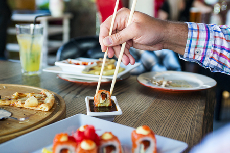 Eating roll sushi in japanese restaurant, hand with chopsticksの写真素材
