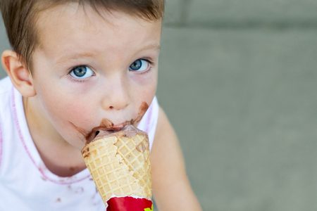 Little kid eats ice-cream in the summer. Cute toddler boy eating ice-cream. Kid with dirty face eating ice creamの写真素材
