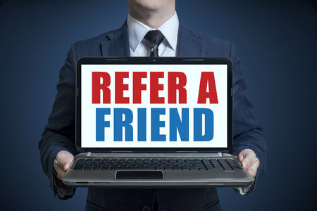 Businessman holding a laptop with text REFER A FRIENDの写真素材