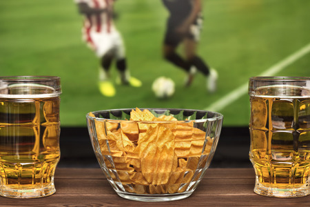 Two glass of cold beer and chips, football match in backgroundの写真素材