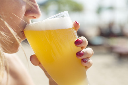 Woman drinking beer with a glass on the beachの写真素材