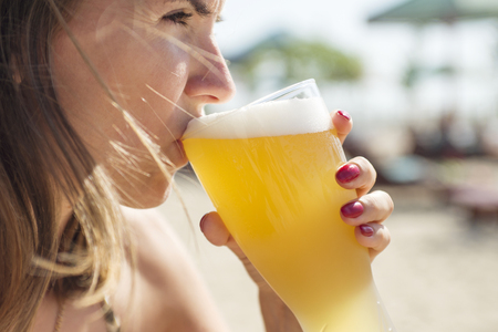 Woman drinking beer with a glass on the beachの写真素材