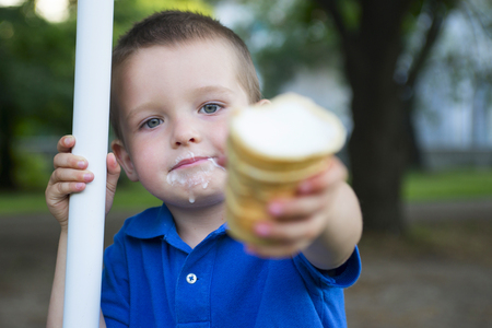 A child holds an ice cream in his outstretched handの写真素材