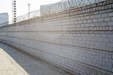Brick fence with barbed wire above. The concept of prison or private property. Barbed wire on a brick wall. Barbed wired fence on the brick wallの写真素材