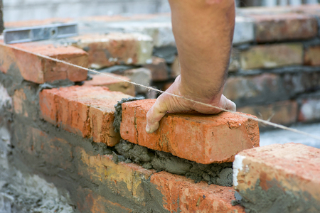 Building brick block wall on construction plant. Worker builds a brick wall in the house. Construction worker laying bricks on exterior wallsの写真素材