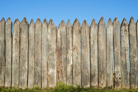 Fence made of sharp wooden stakes against the blue sky. Wooden fence vertical logs pointed against the sky protection against invaders and wild animalsの写真素材