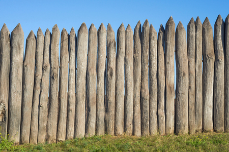 Fence made of sharp wooden stakes against the blue sky. Wooden fence vertical logs pointed against the sky protection against invaders and wild animalsの写真素材