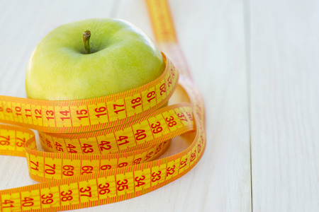 Green apples with measuring tape on white wooden background. Dieting conceptの写真素材