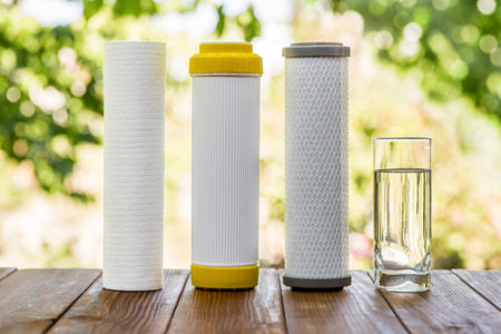 A glass of purified water and filter cartridges on wooden table on green natural backgroundの写真素材