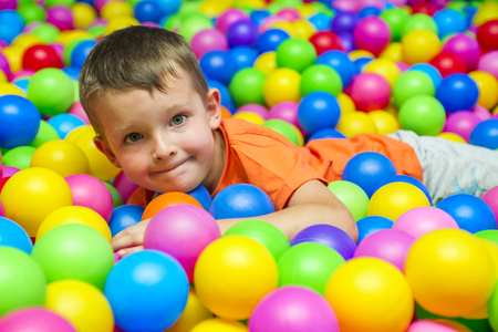 Happy laughing boy having fun in ball pit in kids amusement park and play center. Child playing with colorful balls in playground ball poolの写真素材