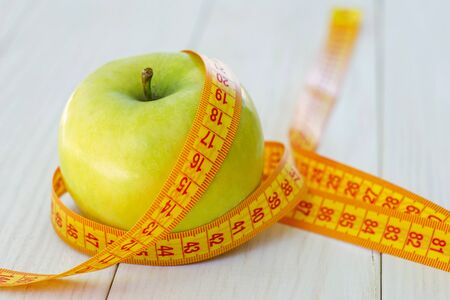 Green apple with measuring tape on wooden background. Apples and sewing tape measure on a wooden table. To lose weight and eat a low calorie apple to lose weightの写真素材
