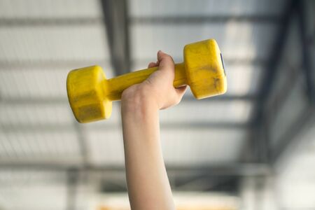 Kid working out with dumbbells  in the sports hall of the club. Child hand holding yellow dumbbell on green backgroundの写真素材
