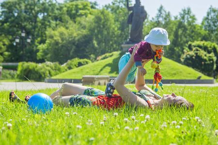 Mother playing with her baby on a great sunny day in a meadow with lots of green grass and wild flowersの写真素材