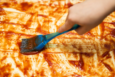 Closeup hand of chef baker making pizza at kitchen. Applying a tomato sauce. Smearing of ketchup on a batterlessの写真素材