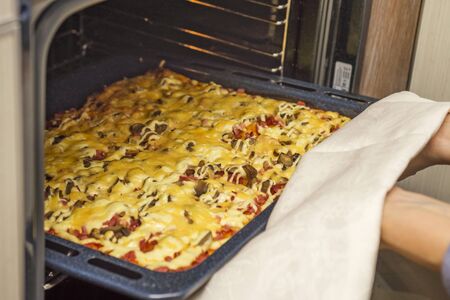 Homemade pepperoni pizza in oven. Delicious pizza cooking in a gas oven. Woman takes a fresh pizza out of the ovenの写真素材