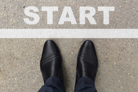 Black shoes of businessman standing at the start line to start or begin new life. Businessman is looking down at his feet on a Asphalt road with start letters painted on the surfaceの写真素材