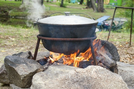 Large metal pot with a lid and handle on tripod used for cooking. Cooking in a bowler hat on the fire in natureの写真素材