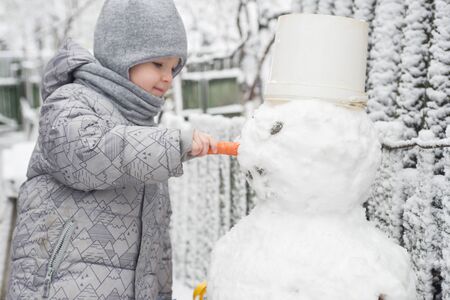 Boy makes a snowman. Adorable kid boy making a snowman, playing and having fun with snow, outdoors on cold day. Active outdoors leisure with children in winterの写真素材